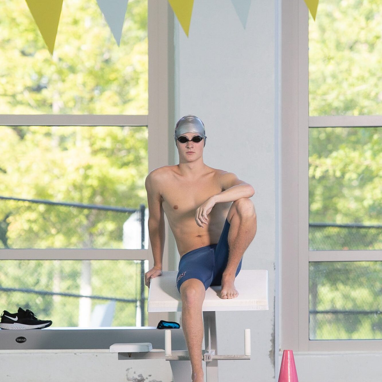 Woodstock High School senior swimmer wearing his swim cap, goggles, and speedo while sitting on the diving block