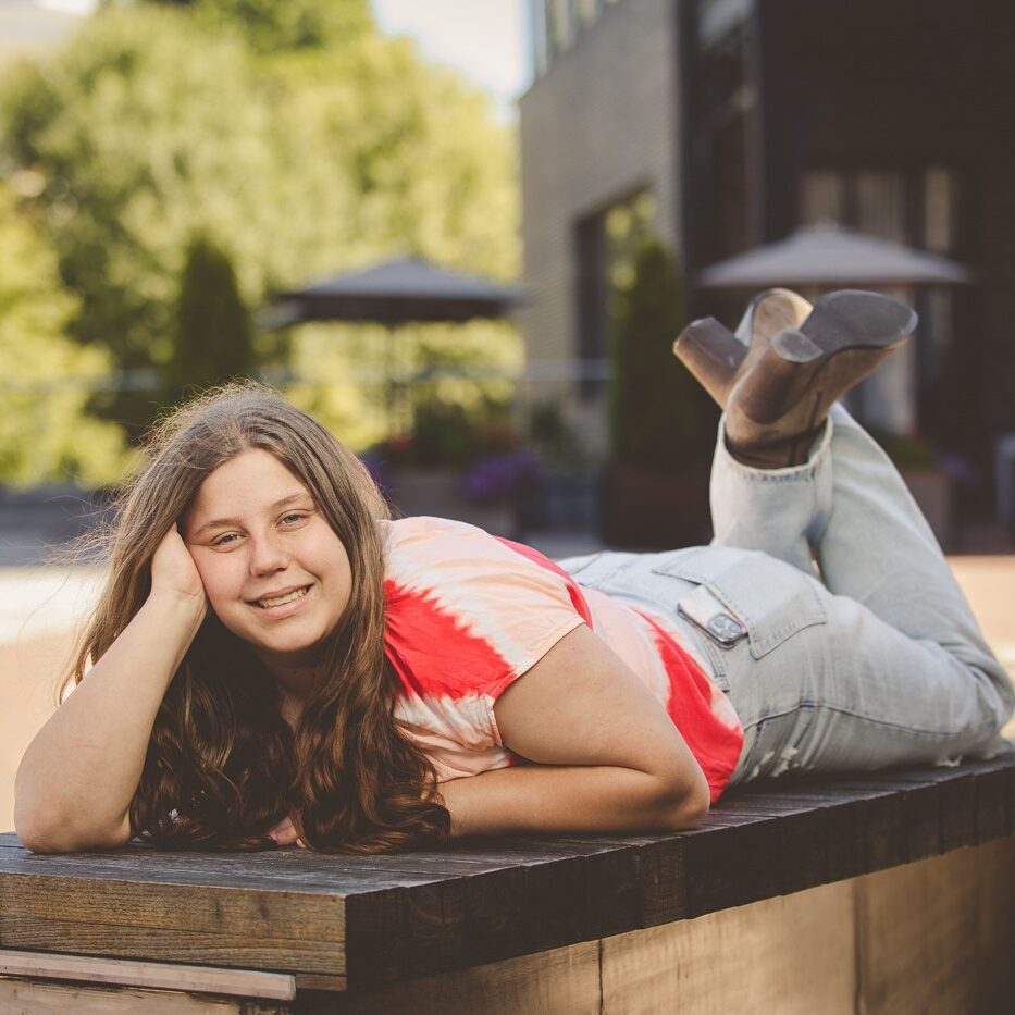 Sweet high school senior girl with long hair laying on a park bench and smiling in Chattanooga