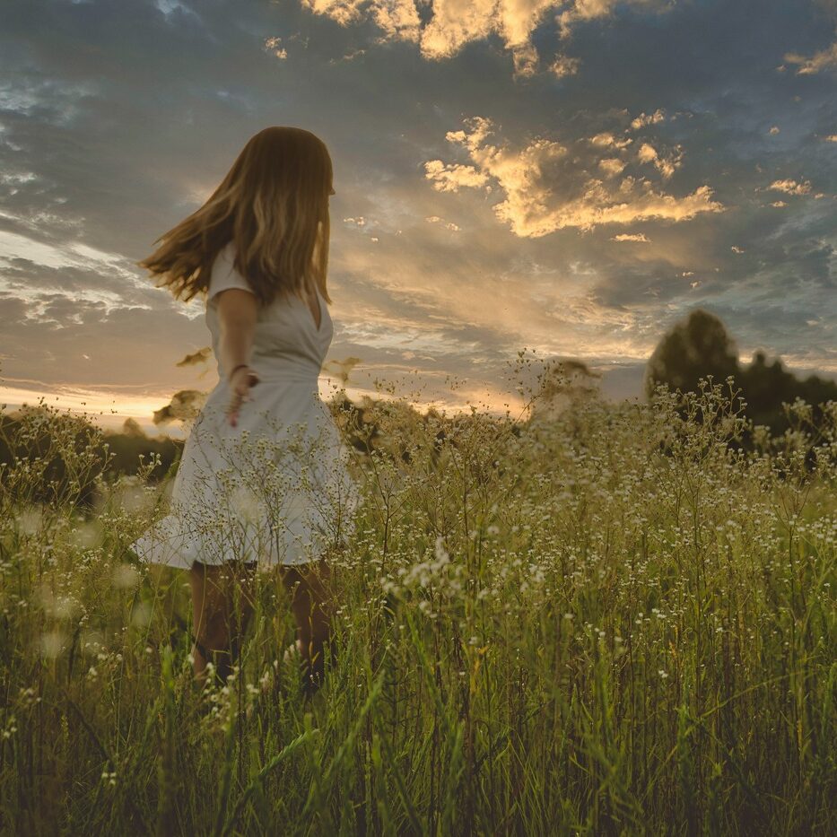 Teenage girl wearing a white dress twirling in a field of wild flowers at sunset