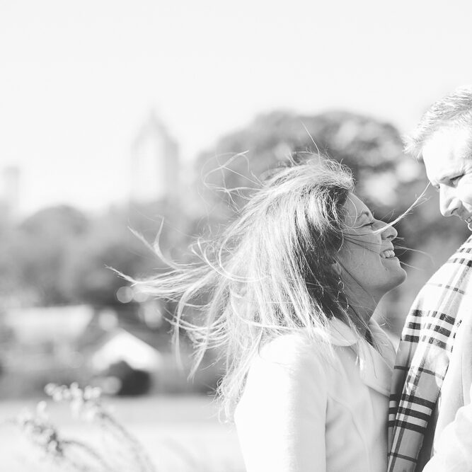 Black and white photograph of engaged older couple with wind blowing her hair around