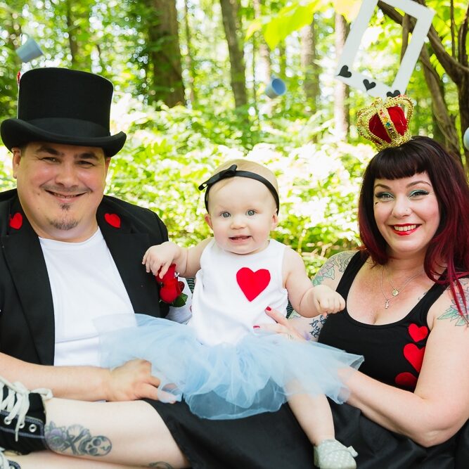 Smiling parents and one year old baby girl all dressed up in Alice in Wonderland theme